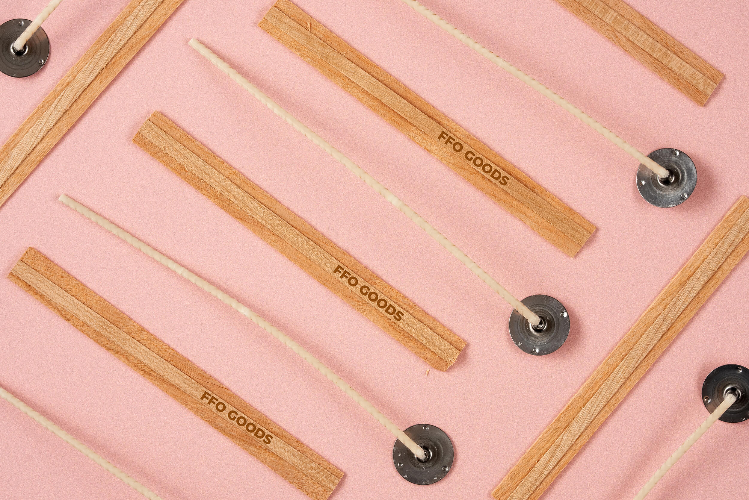 Wooden candle wicks with metal bases, labeled FFC GOODS, are arranged diagonally on a pink background.