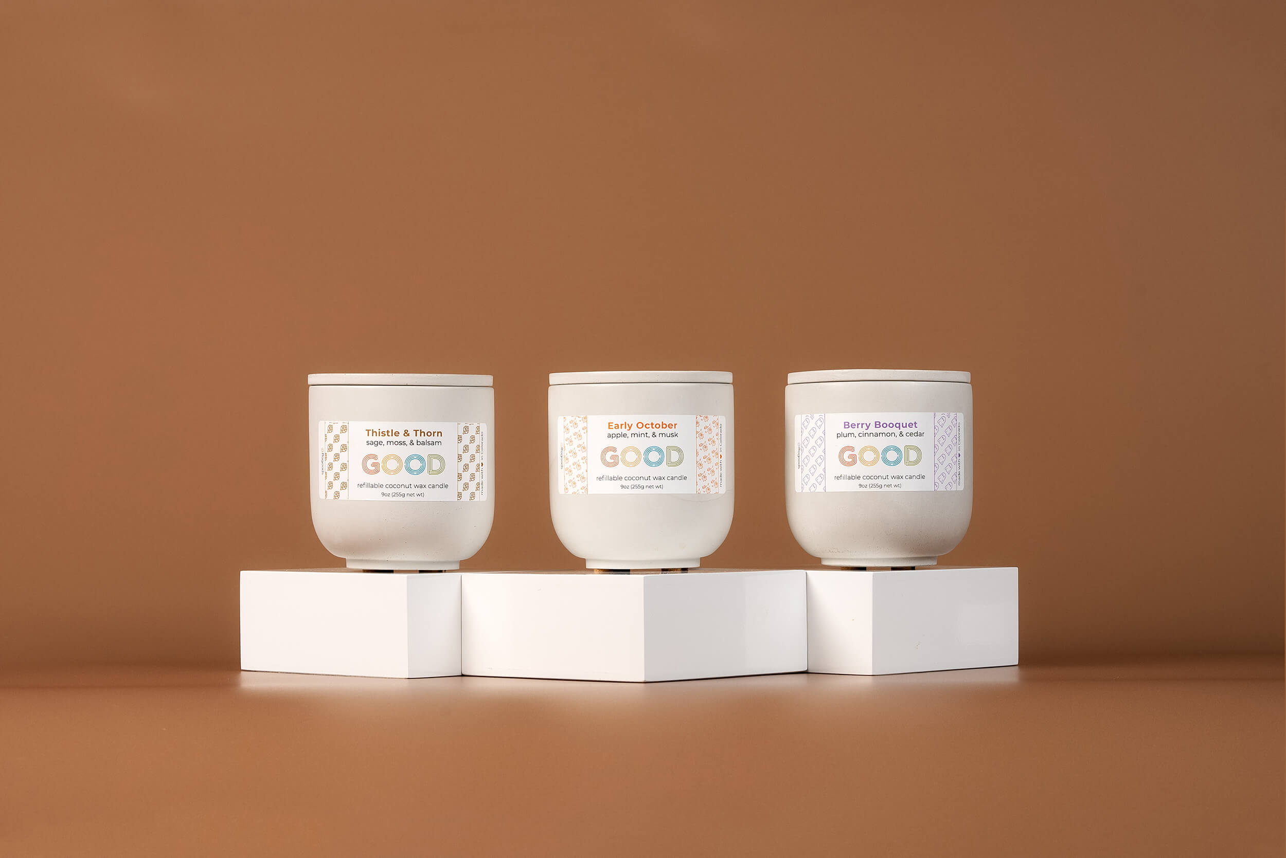 Three lit candles on white blocks surrounded by autumn leaves, cupcakes, and decorative items against an orange background.