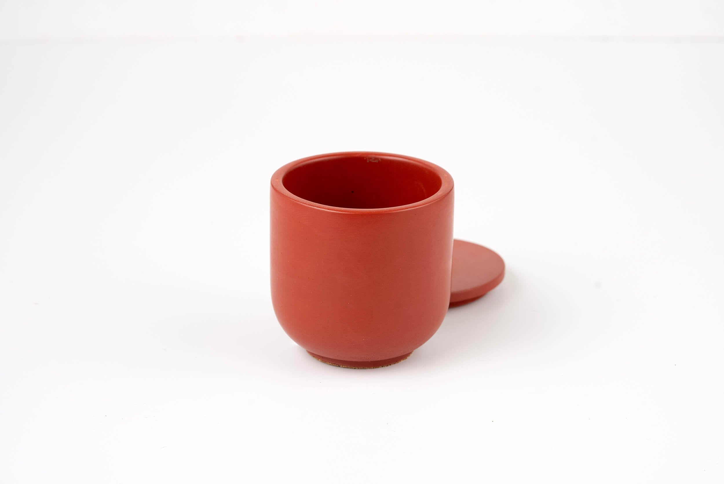 A small, round, red Lava Candle Vessel with a matching lid sits beside it on a plain white background.