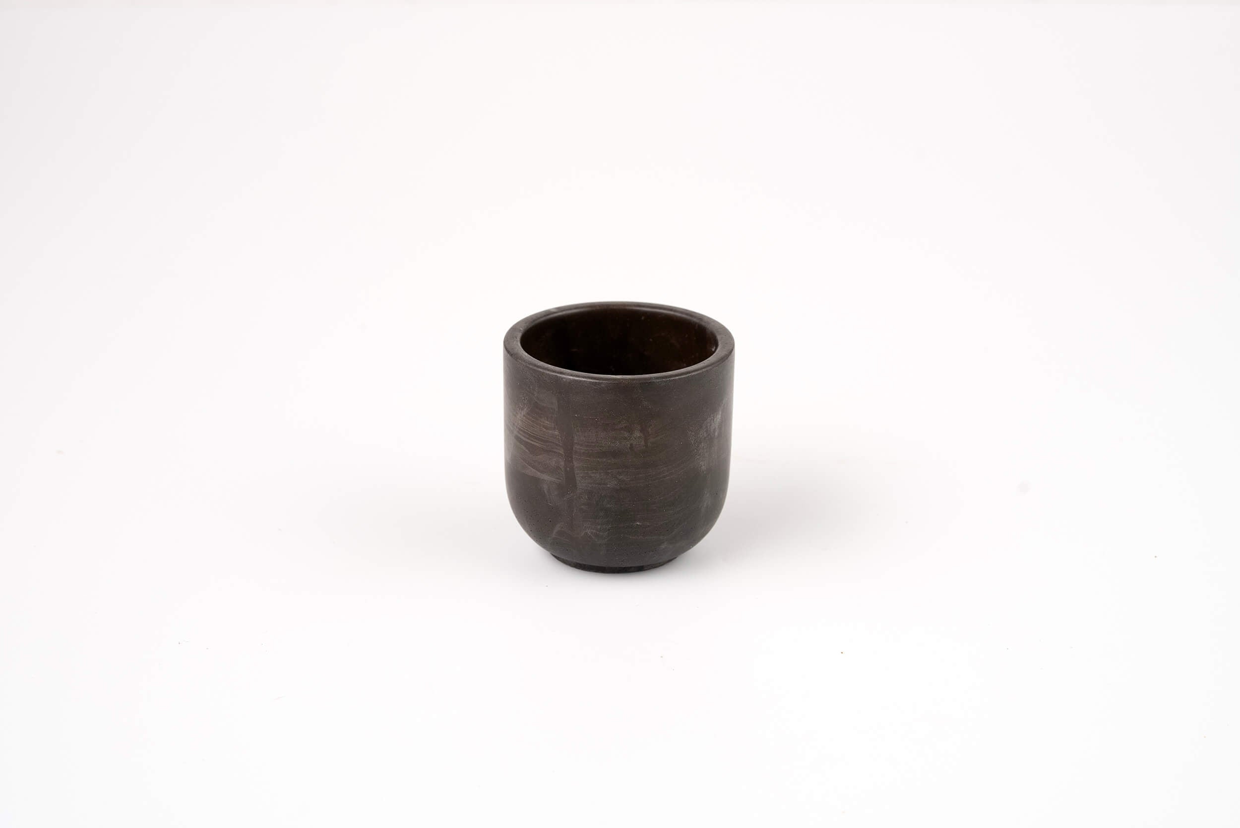 The Graphite Candle Vessel is a small, dark ceramic cup with a smooth, round shape and minimalist design, shown on a plain white background.