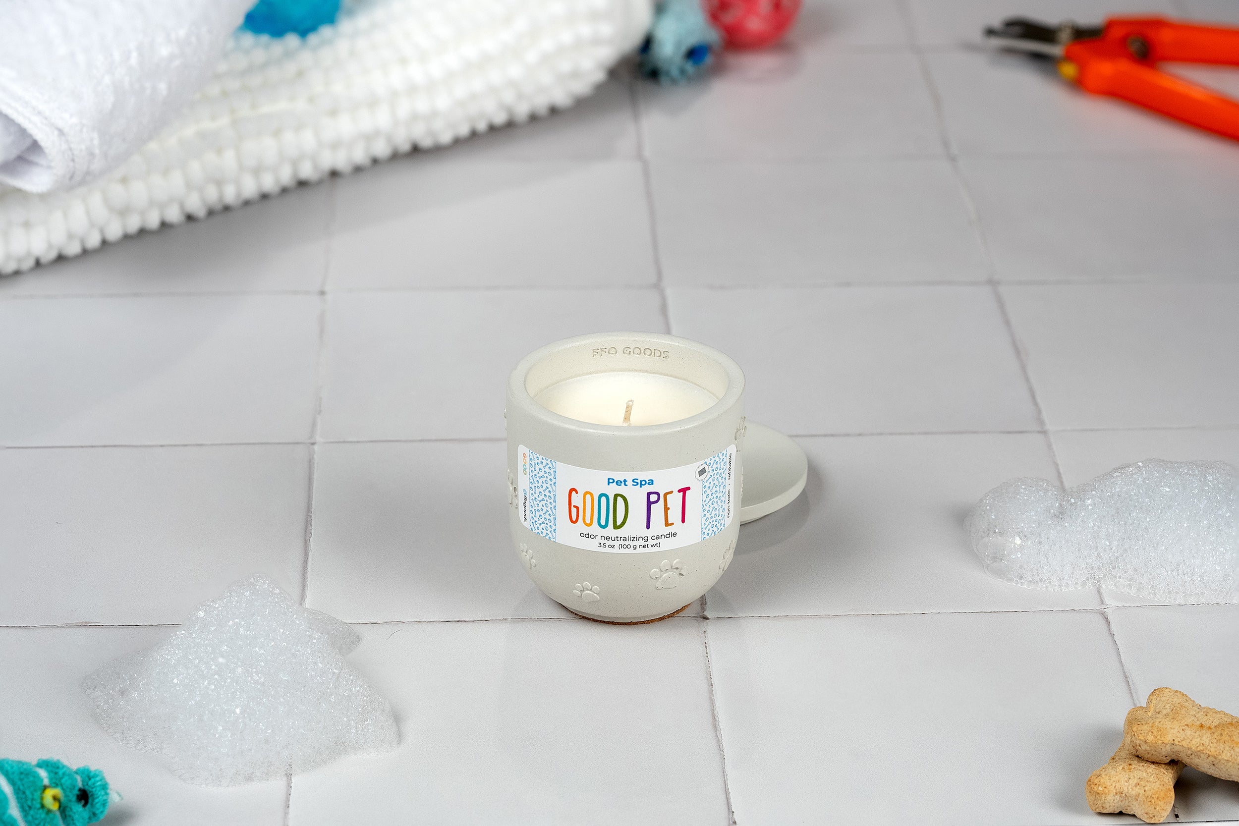 The Pet Spa candle, displayed in its refillable concrete vessel on tiles and surrounded by bubbles, treats, a towel, grooming scissors, and toys, creates a calming spa vibe with soothing, odor-eliminating scents for your pet.