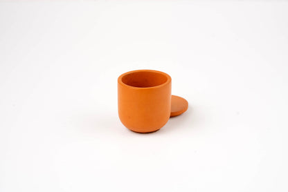 The Orange Lilly Candle Vessel, small and round with a matching lid, is displayed against a plain white background.