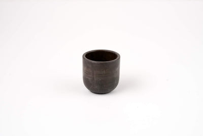 The Graphite Candle Vessel is a small, dark ceramic cup with a smooth, round shape and minimalist design, shown on a plain white background.