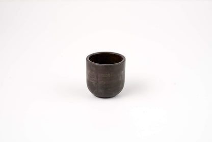 The Graphite Candle Vessel is a small, dark ceramic cup with a smooth, round shape and minimalist design, shown on a plain white background.