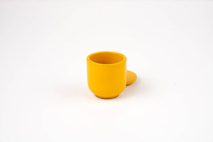 The Marigold Candle Vessel is a small, round, yellow container with a matching yellow lid behind it, displayed against a plain white background.