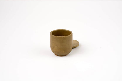 The Bark Candle Vessel is a small, light brown ceramic cup with a matching lid placed slightly behind it on a plain white background—ideal for elegantly holding your favorite candle scents.