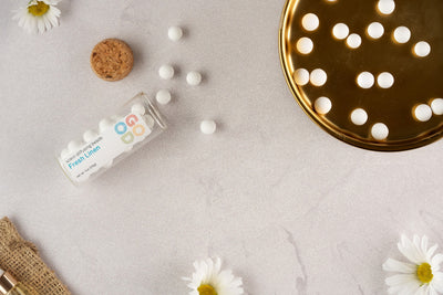 A glass bottle labeled Scent Diffusing Ceramic Beads spills ceramic fragrance beads onto a light surface. Some beads rest in a gold dish, with a cork, burlap, and white daisies nearby—an eco-friendly air freshener with long-lasting scent.