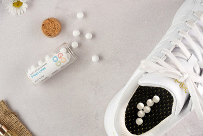 Scent Diffusing Ceramic Beads labeled "Fresh Linen" spill near and inside a white sneaker, surrounded by white round mints, a cork, flower, and burlap on a light textured surface for long-lasting fragrance.