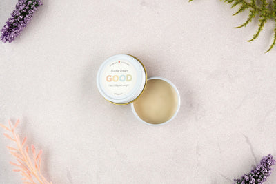 An open tin of Cuticle Cream rests on a light, textured surface with sprigs of lavender and greenery nearby, emphasizing its natural ingredients for luxurious nail care.