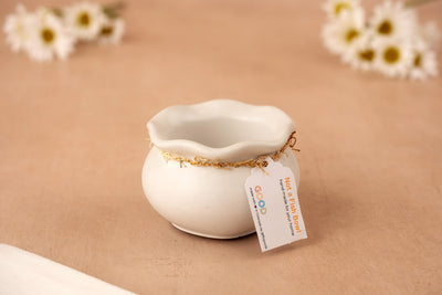 The Not a Fish Bowl – Modern Twist on a Classic Shape is a small, round white concrete accent bowl with a wavy rim, featuring a gold string and "Not a Fish Bowl" tag. White flowers blur in the background on a beige surface.
