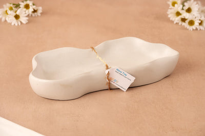 The Wavy Tray – Modern Concrete Catchall sits on a beige surface, accented by white daisies in the background and corner, creating a soft, elegant scene that highlights this modern tray’s timeless appeal.