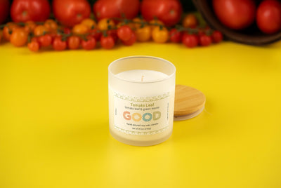 The Tomato Leaf candle with a wooden lid rests on a yellow surface among cherry and large tomatoes, filling the air with a fresh garden scent.