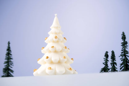 The Christmas Tree Shaped Candle, crafted from soy beeswax and adorned with small gold ornaments, stands on a snowy surface with miniature evergreens in the background—a perfect holiday decor accent.