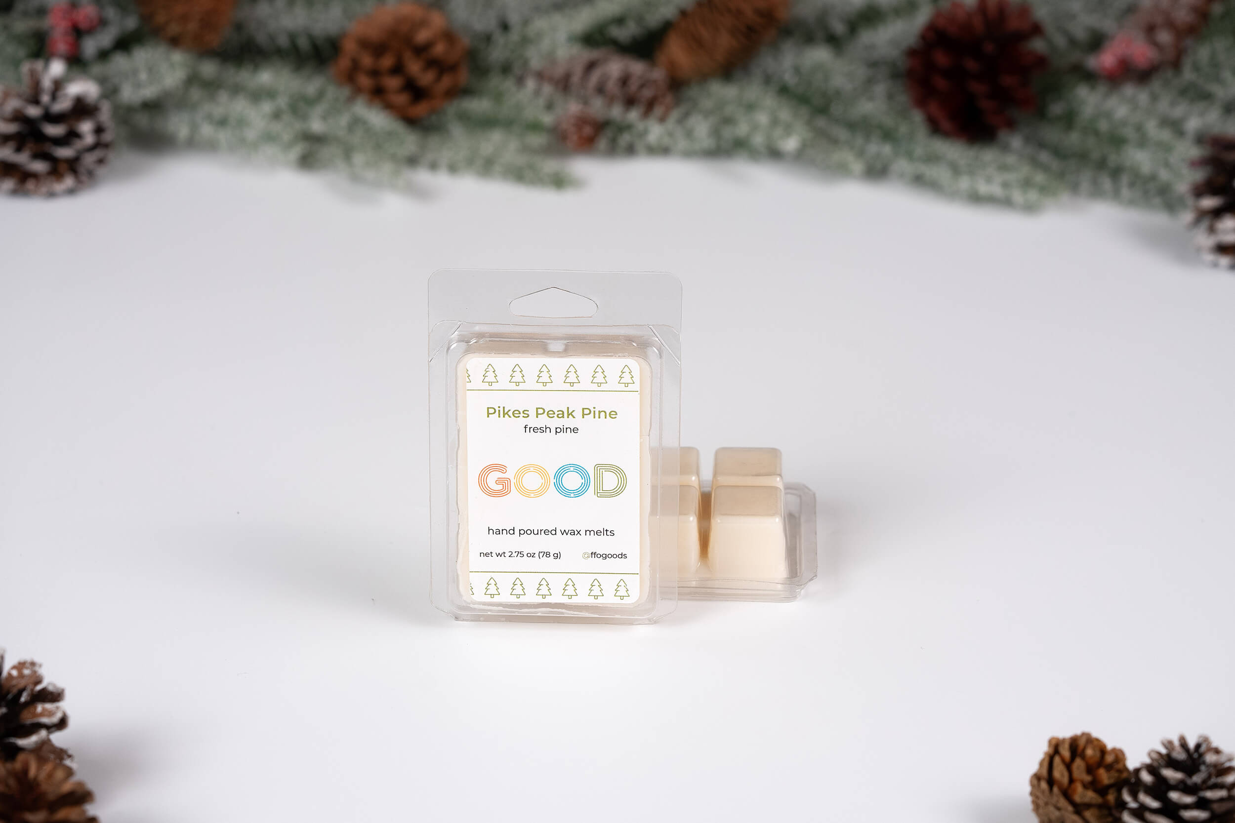 Pikes Peak Pine Wax Melts, inspired by true Colorado scents, are shown with pinecones and greenery. The open clamshell holds several off-white cubes, ideal for your wax melter.