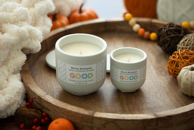 Two white coconut wax candles in concrete jars labeled Berry Booquet sit on a wooden tray with fall decor—pumpkins, leaves, and twine balls. Enjoy phthalate-free fragrances for a cozy, inviting atmosphere.