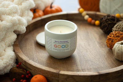 A white coconut wax candle labeled "Berry Booquet" sits on a wooden tray with autumn accents—pumpkins, cozy fabric, and twine balls. Enjoy its phthalate-free fragrance all season.