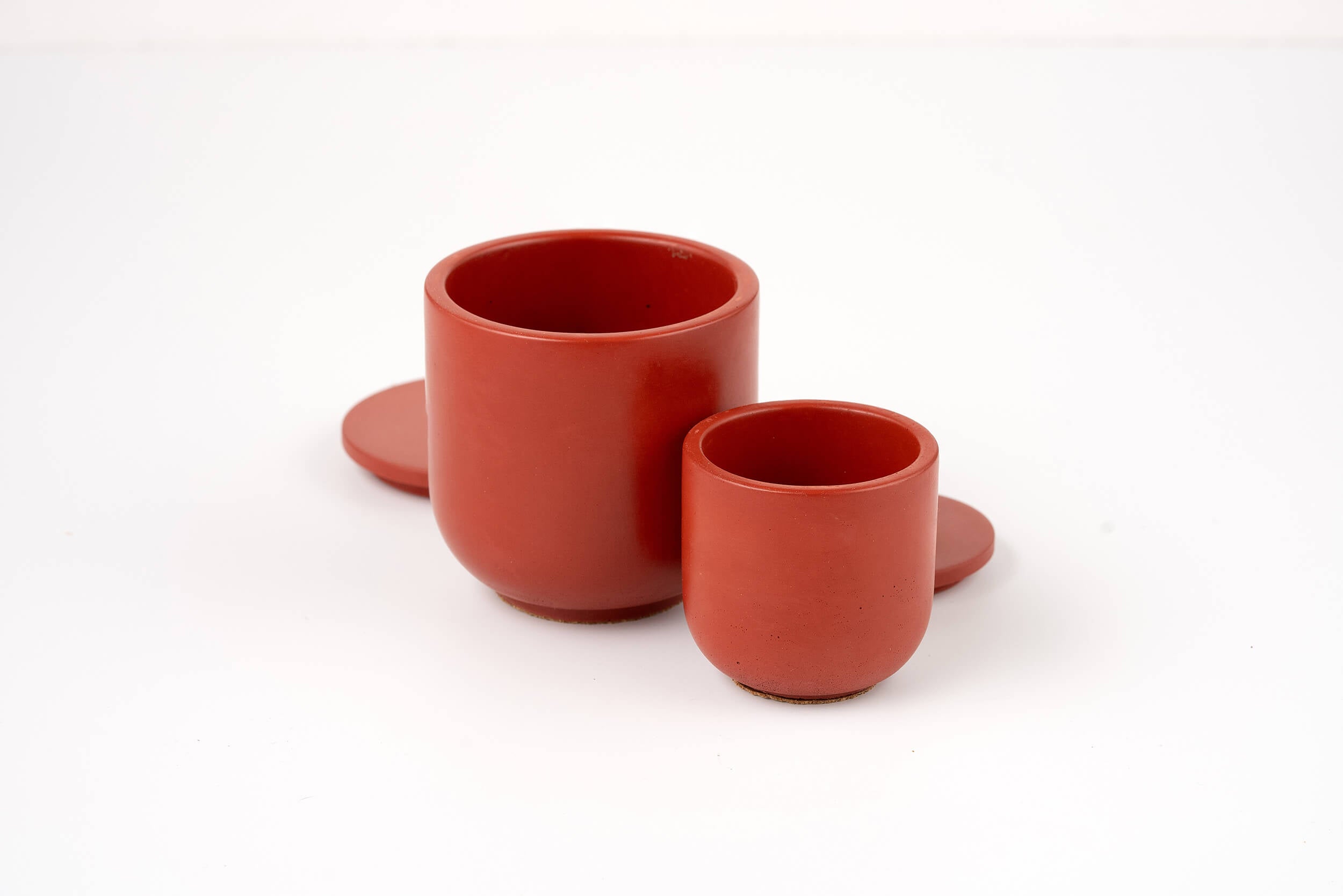 Two Lava Candle Vessels in red are displayed on a white background, each with a matching round coaster. The smaller vessel sits in front and slightly to the right of the larger one.