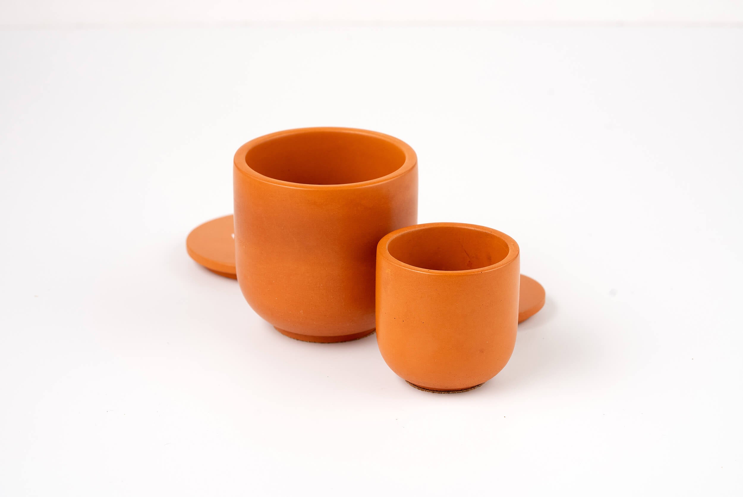 Two Orange Lilly Candle Vessel containers in different sizes sit side by side on a white surface, with their matching round lids placed behind them.